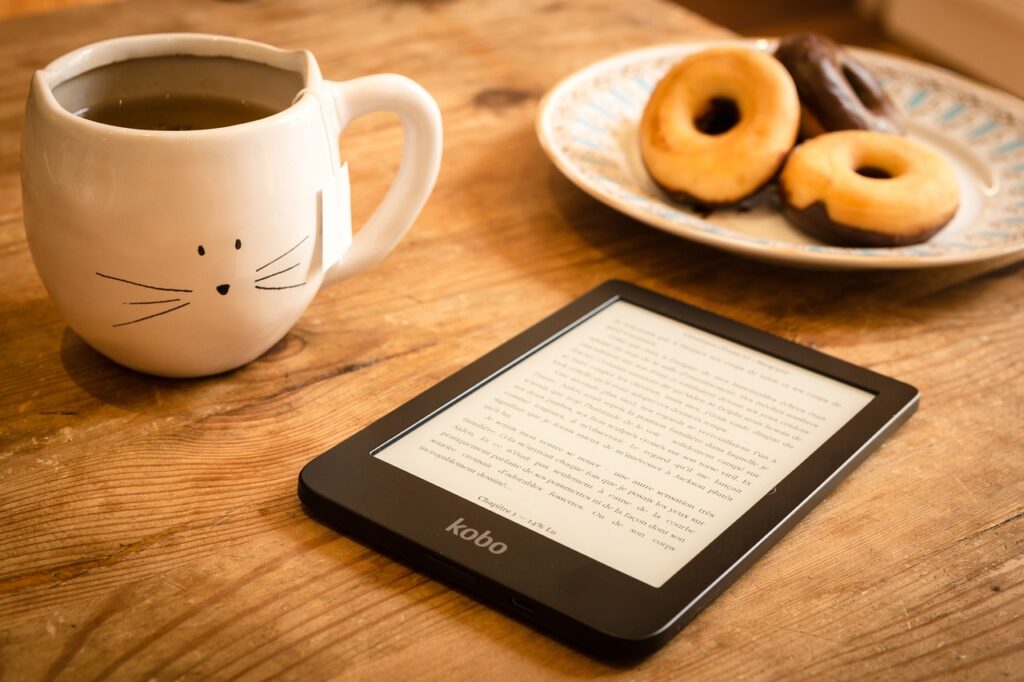 An image of a digital book reader with cookies and tea on the table.