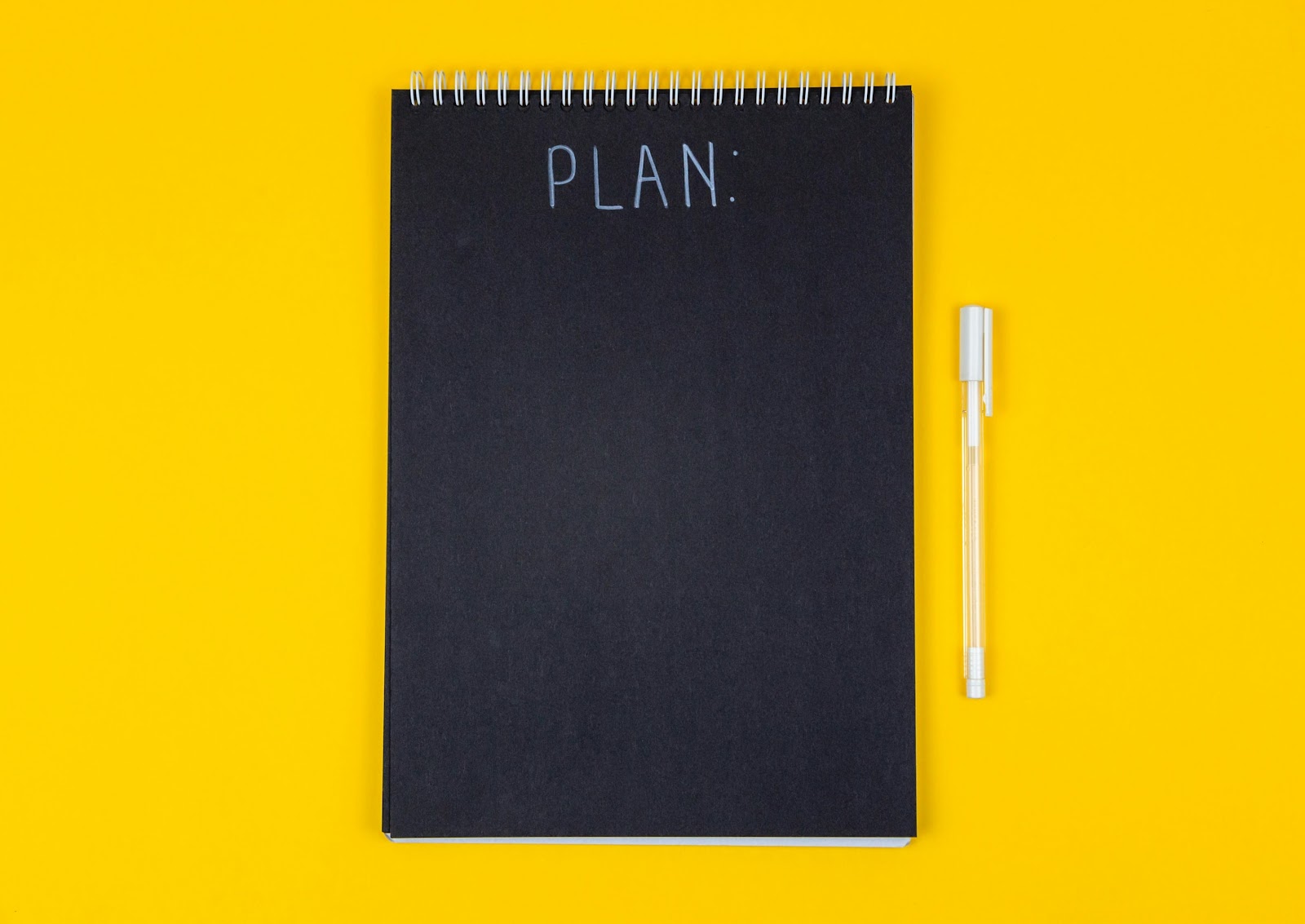 An image of a black notepad with "plan" written on it and a pen beside it.